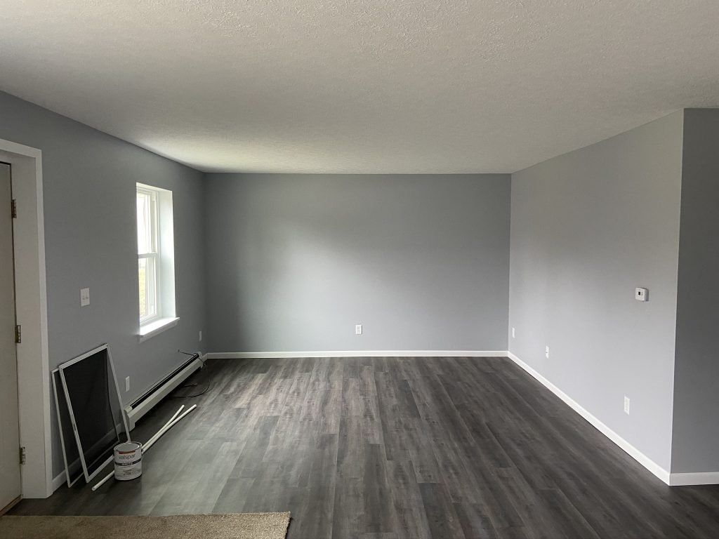 An empty living room with hardwood floors and gray walls.
