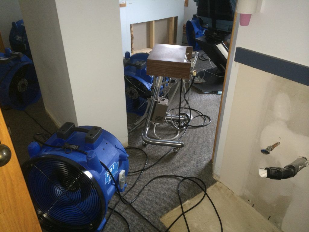 A room with a lot of wires hanging from the ceiling and a blue industrial fan.