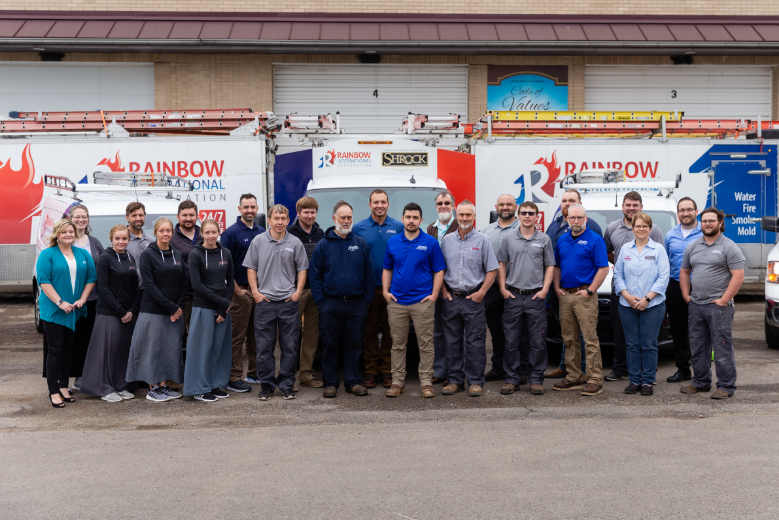 A group of people are posing for a picture in front of Rainbow Restoration trucks.