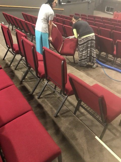 Two people are cleaning red chairs in an auditorium.