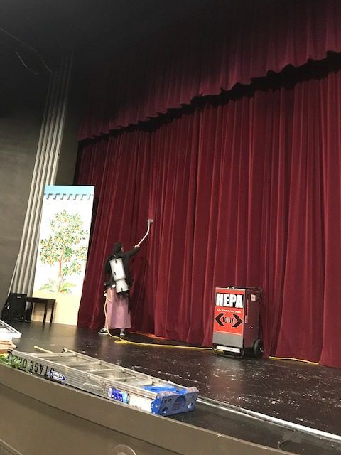 A woman is standing on a stage cleaning the curtains.