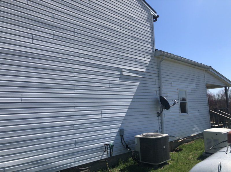 A white house with siding, a central air unit and satellite dish attached.