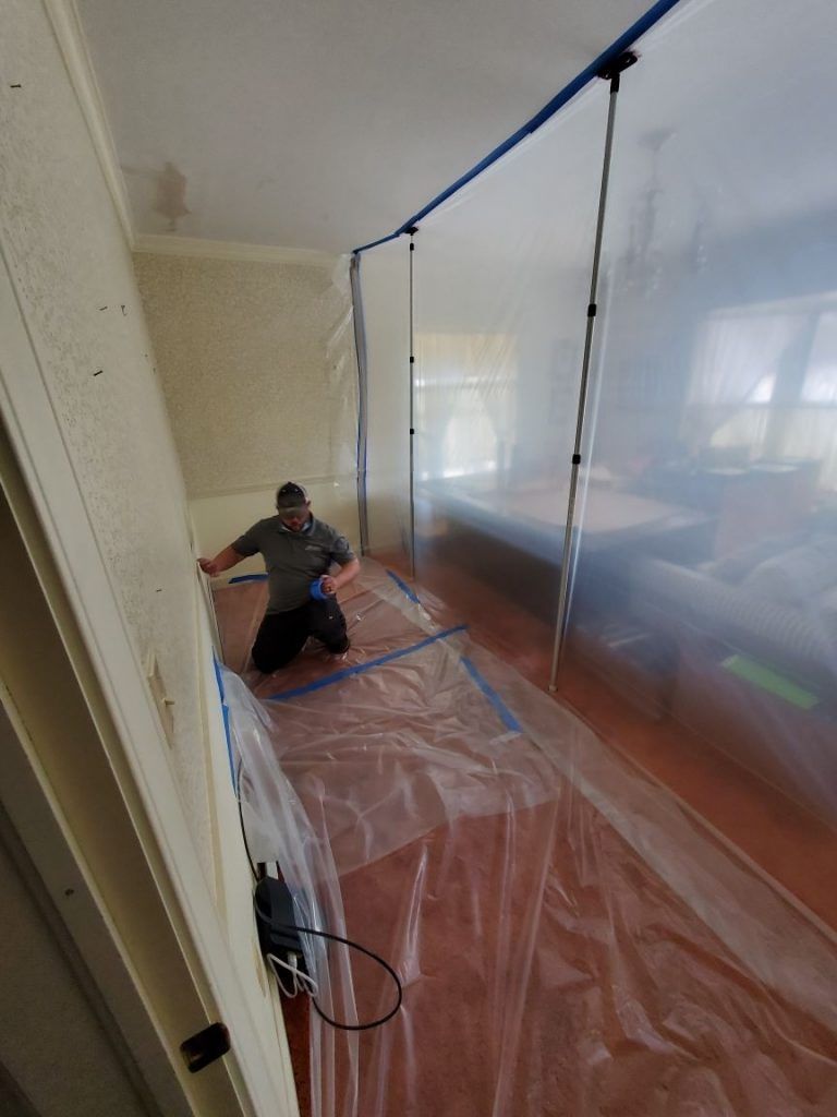 A man is repairing a water damaged room covered in plastic.