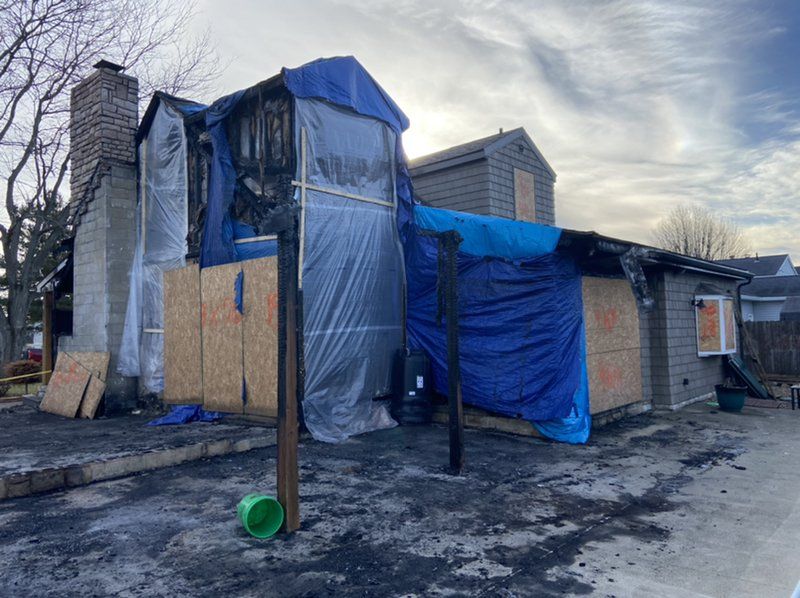 A house that has been damaged by a fire is covered in blue tarps.