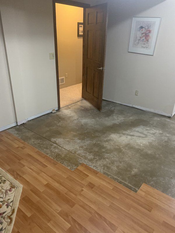 A water damaged room with hardwood floors and a door leading to a bathroom.