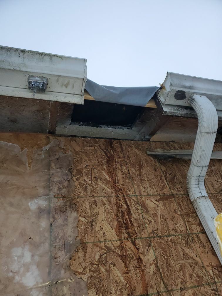 A house with chimney fire damaged roof and a hole in it and a gutter on it.