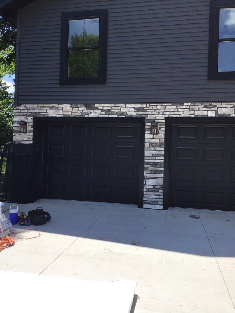 A house with three black garage doors and a stone wall.