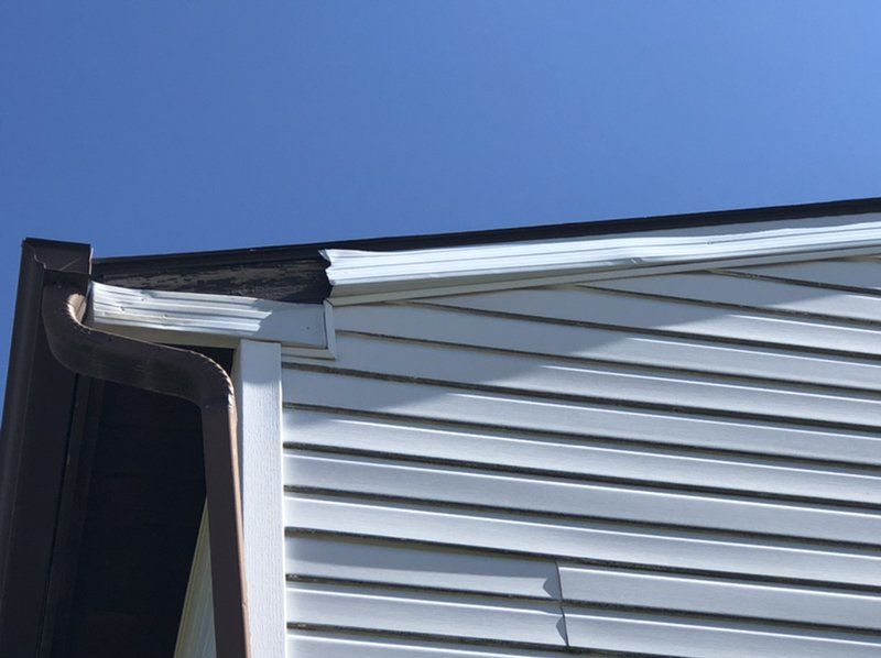 A white house with a brown gutter and a blue sky in the background.