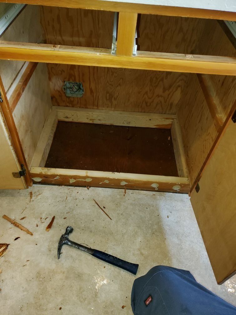 A hammer is laying on the floor next to a cabinet.