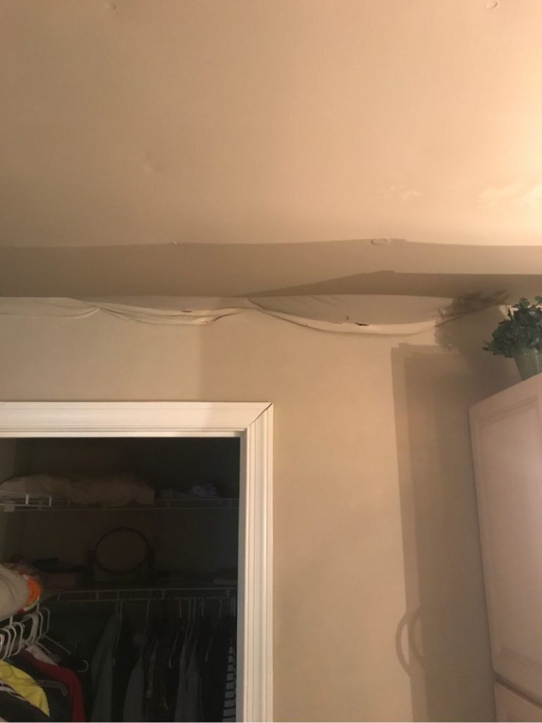 A closet with clothes hanging on a rack and a ceiling with a drain coming out of it.