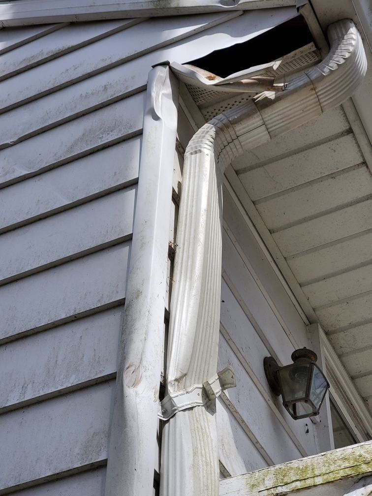 A white house with a broken gutter on the side