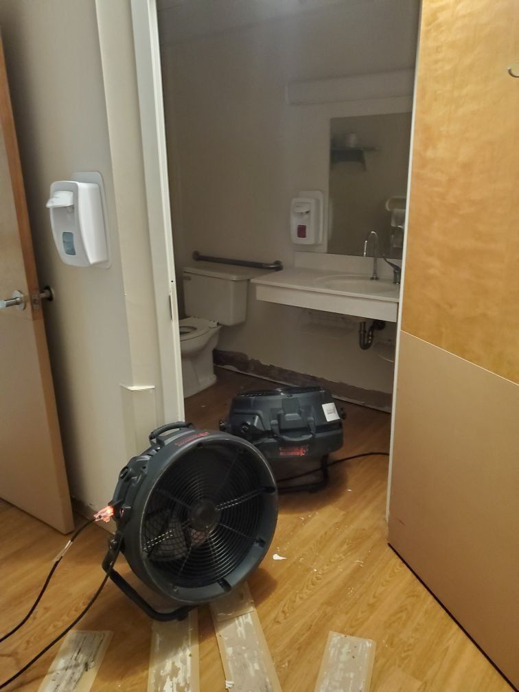 A fan is sitting on the floor in a water damaged bathroom next to a toilet.