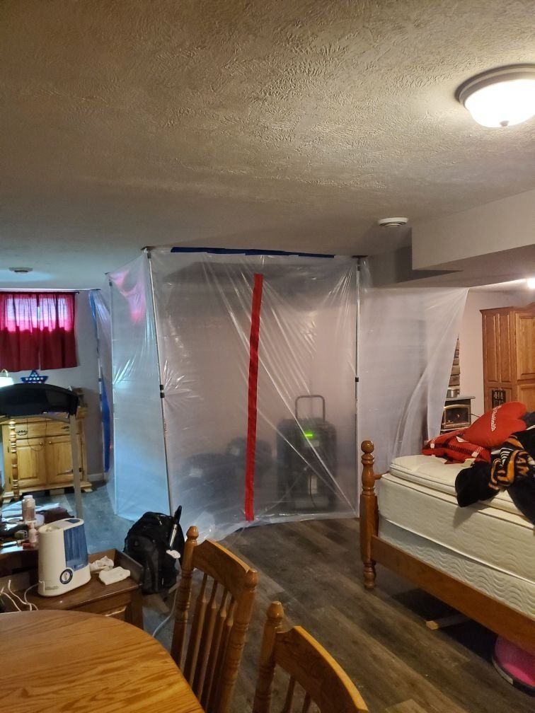 A room with a table , chairs , and a bed covered in plastic.