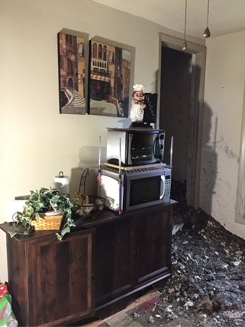 A living room with fire damage, a microwave, and a broken glass floor.