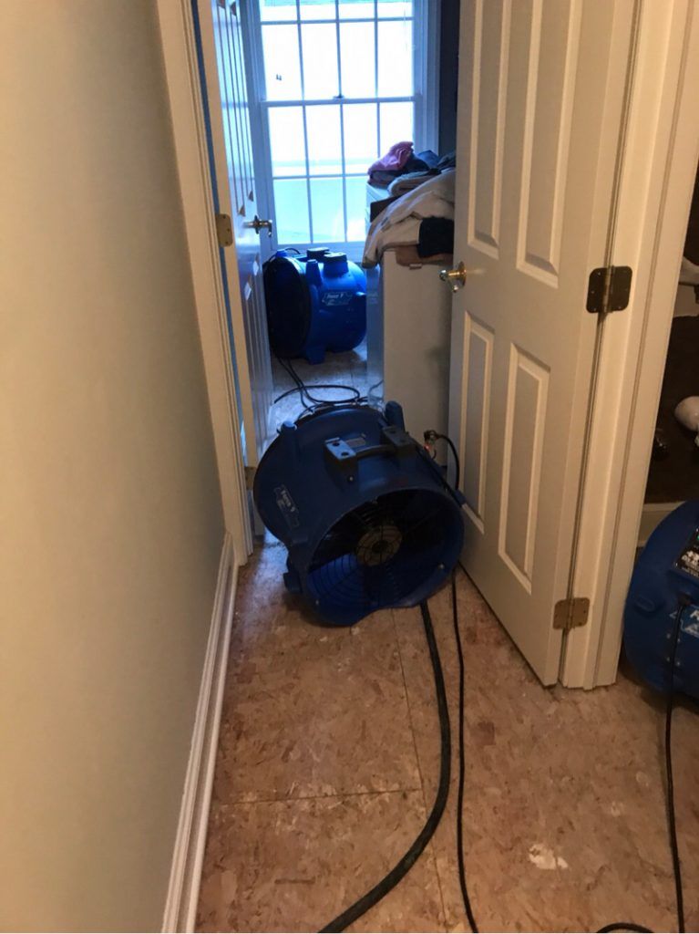 An industrial blue fan is sitting in a hallway next to a door.