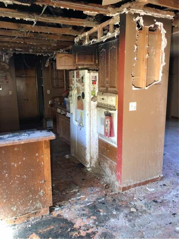 A fire damaged kitchen with a refrigerator, cabinets, and a broken ceiling.