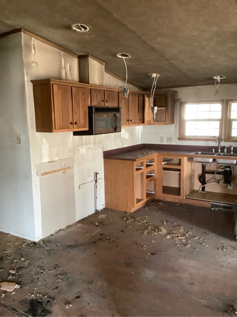 A fire damage kitchen with wooden cabinets and a microwave.