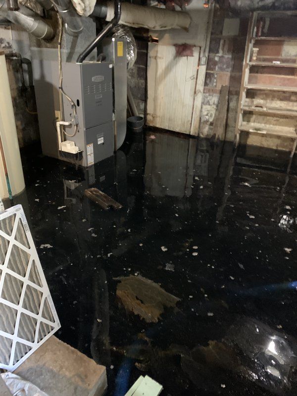 A flooded basement with a furnace and stairs.
