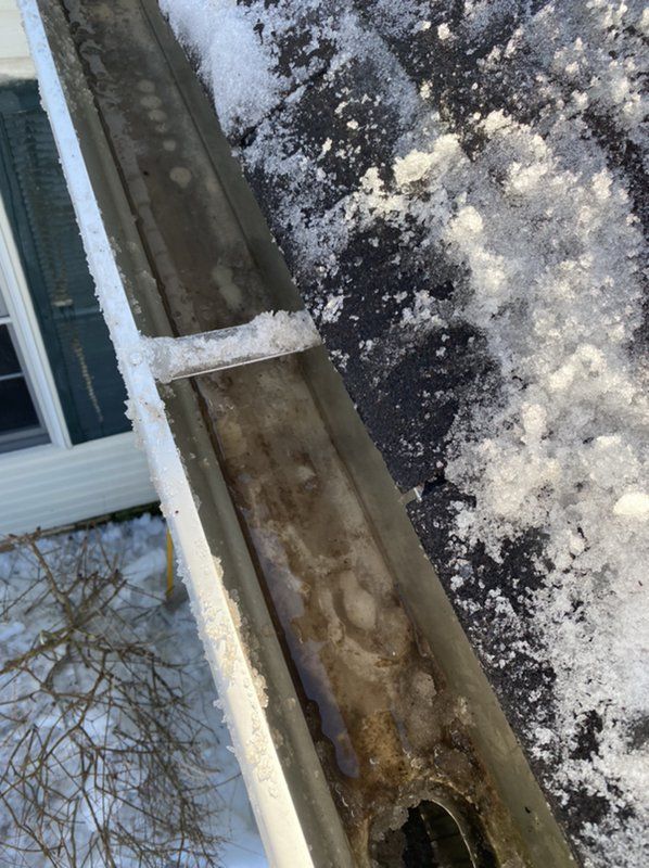 A close up of a gutter with snow on it and a house in the background.