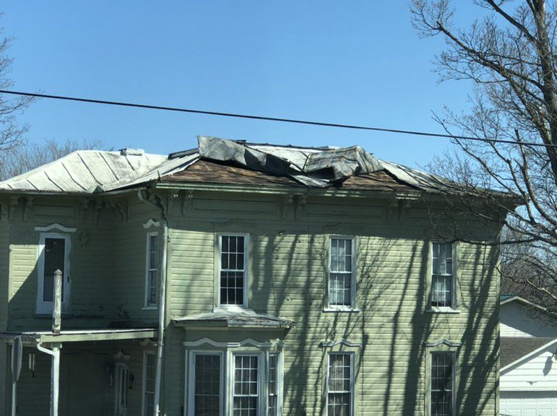 A green house with a roof that has been damaged by a storm.