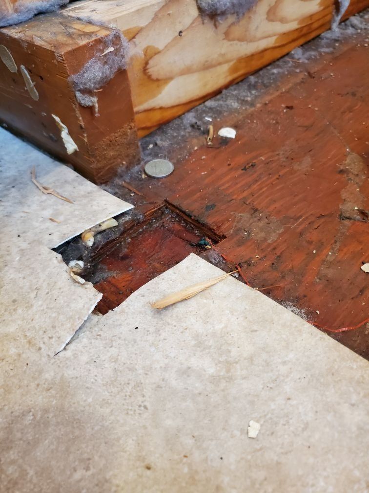 A damaged wooden floor with a hole in it and a piece of paper on it.