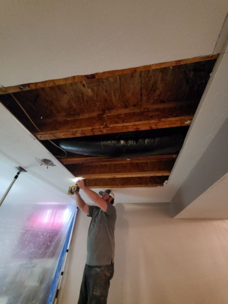 A man is repairing the ceiling of a room with a drill.