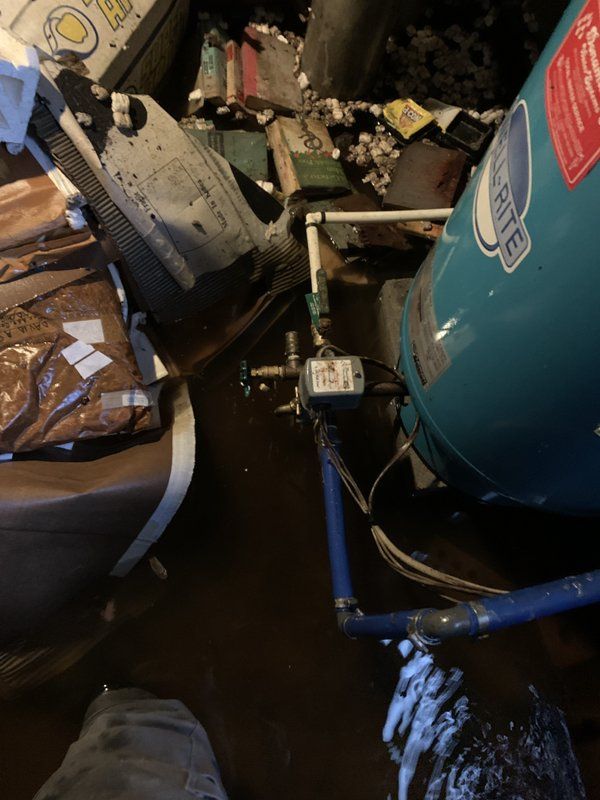 A person is standing in a flooded room next to a water tank.