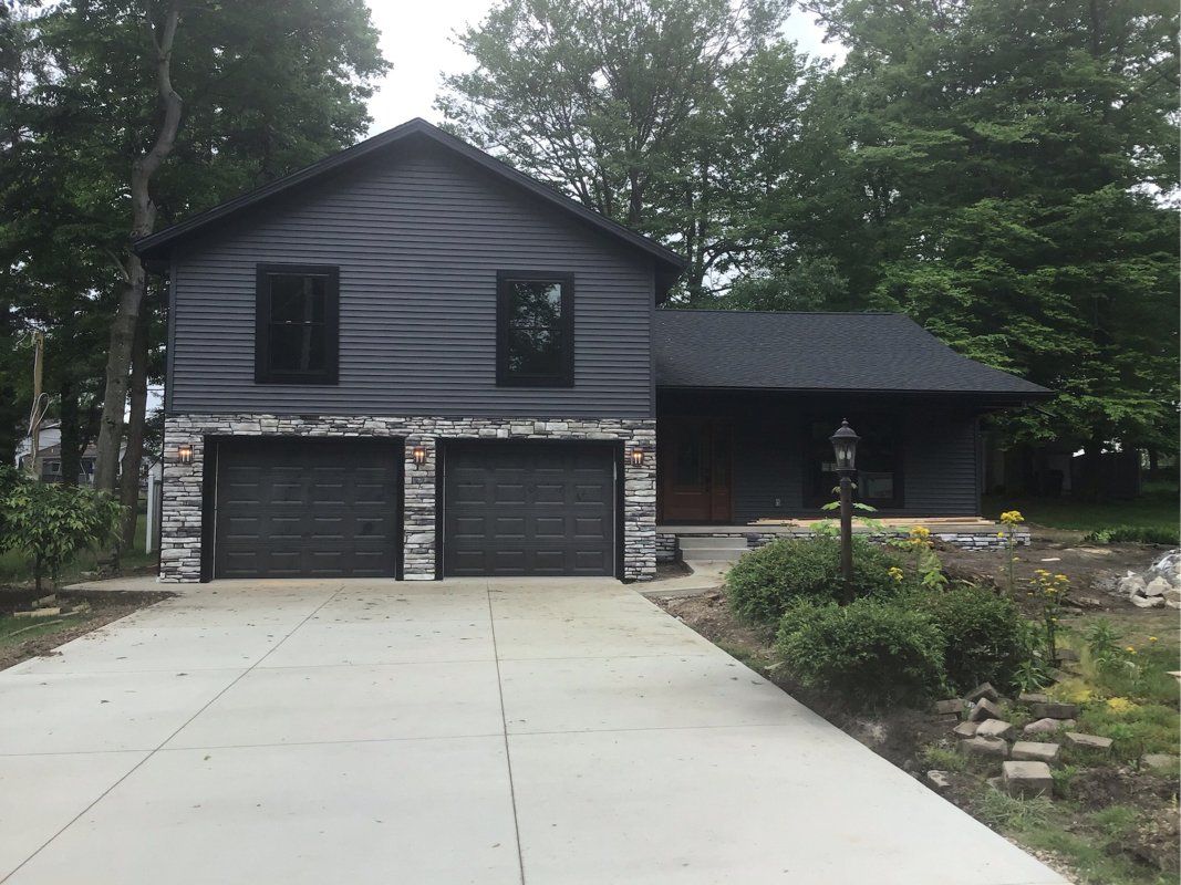 A black house with two garage doors and a driveway.