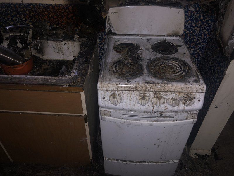 A dirty stove is sitting in a kitchen next to a sink.