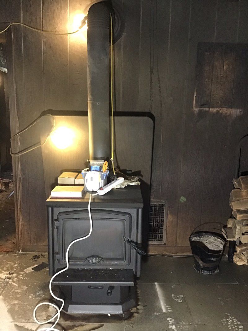 A wood stove is sitting in a dark room next to a wall.