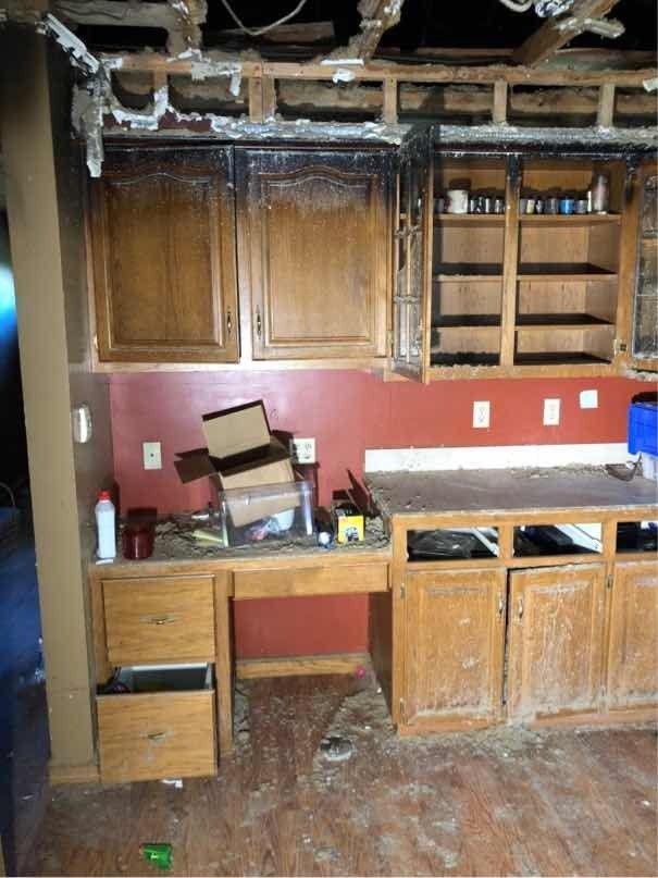 A fire damaged kitchen with wooden cabinets and a desk.