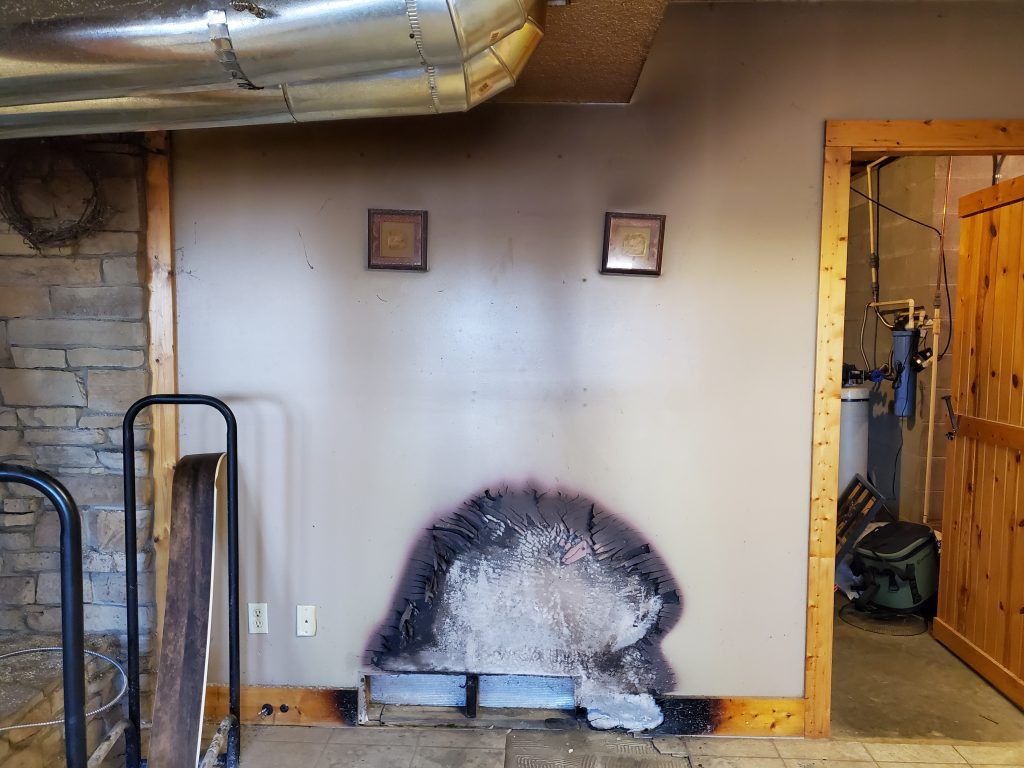 A room with a brick wall that has been damaged by fire.