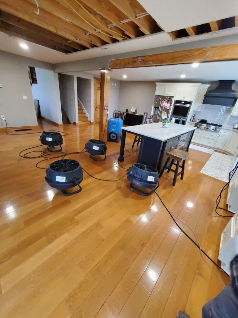 A living room with hardwood floors, a table, and four industrial fans inside.
