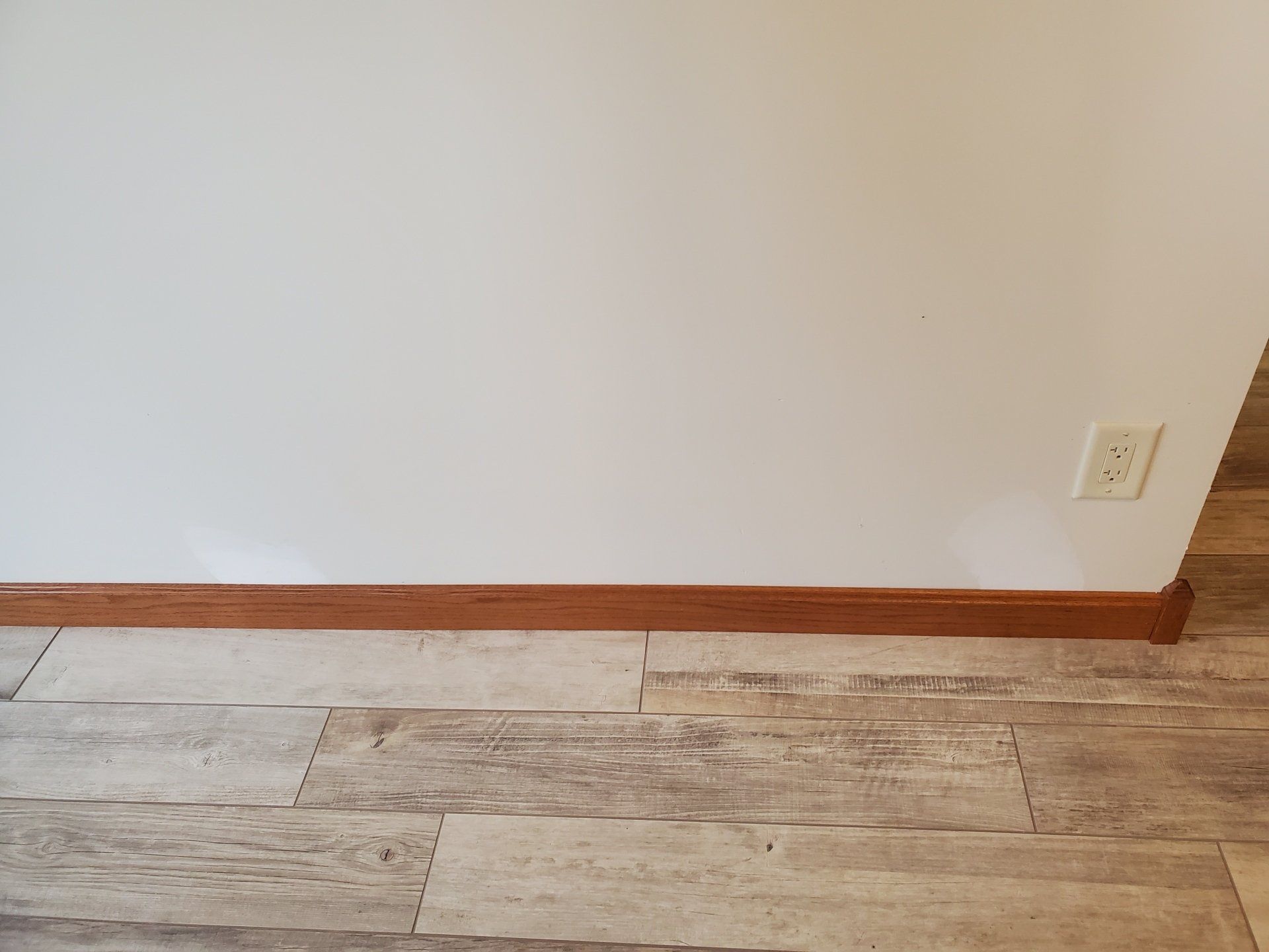 A white wall with a wooden trim and a wooden floor in a room.