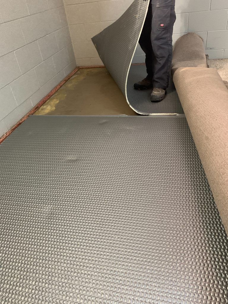 A person is rolling a roll of carpet on a floor.