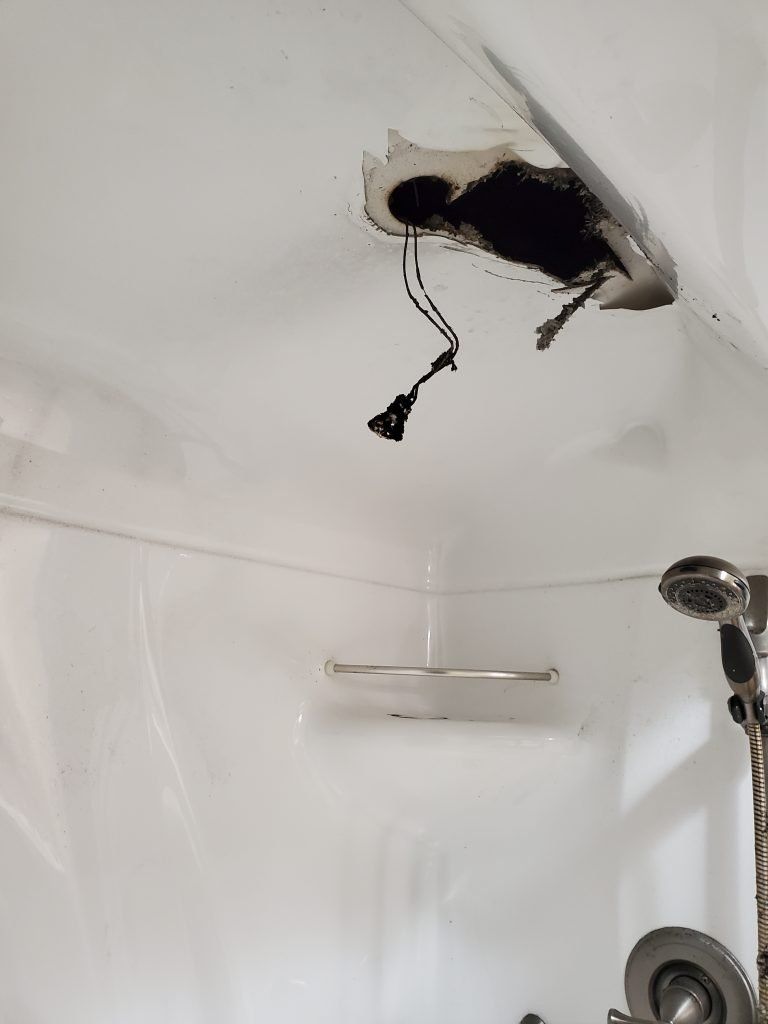 A shower with a hole in the ceiling and a shower head