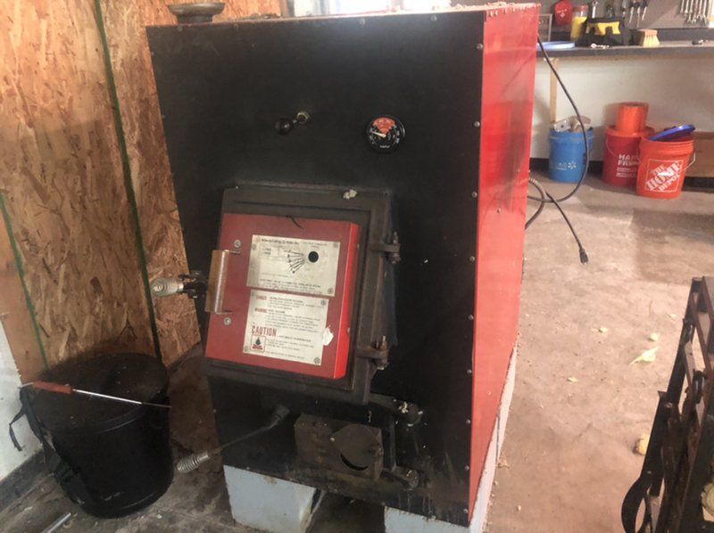 A red and black wood stove is sitting in a garage with fire damage.