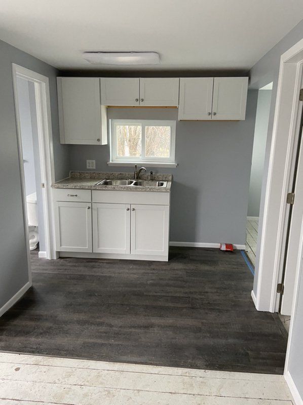 A kitchen with white cabinets , a sink , and a window.