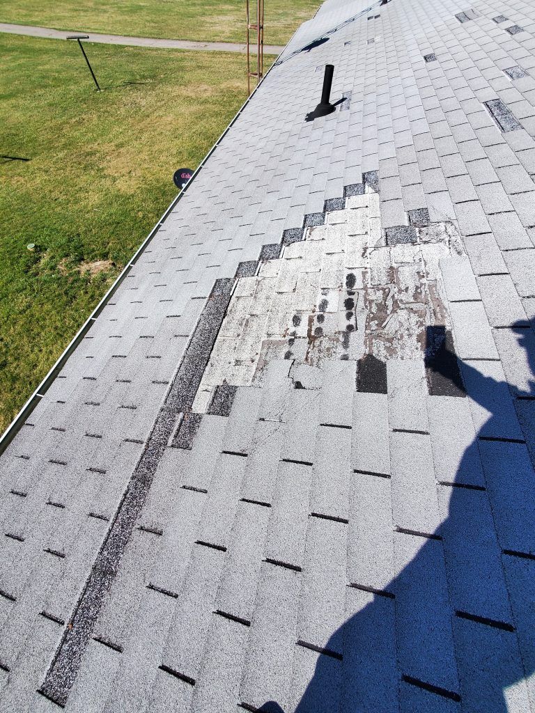 A water damaged roof with missing shingles and a shadow of a person on it.