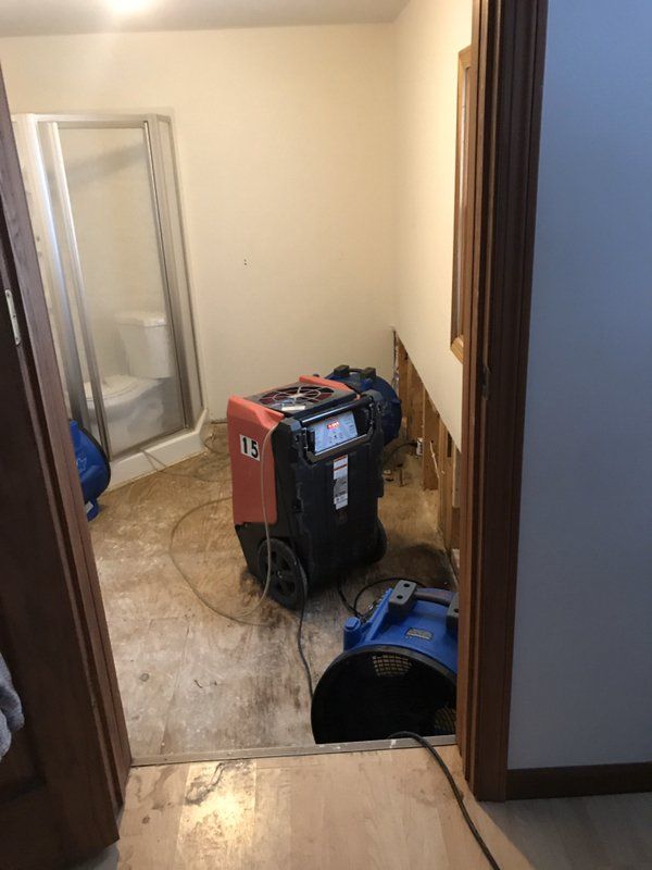 An industrial machine and blue fan are sitting on the floor in a bathroom next to a shower.