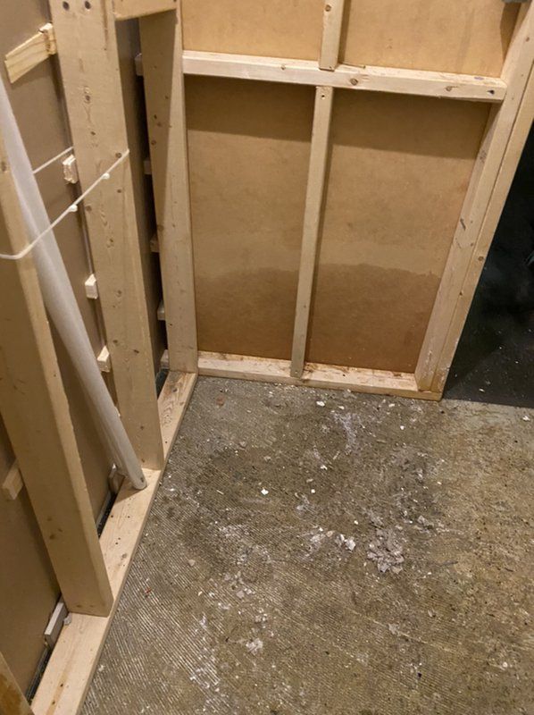 A room with a wooden wall and a concrete floor damaged by water.