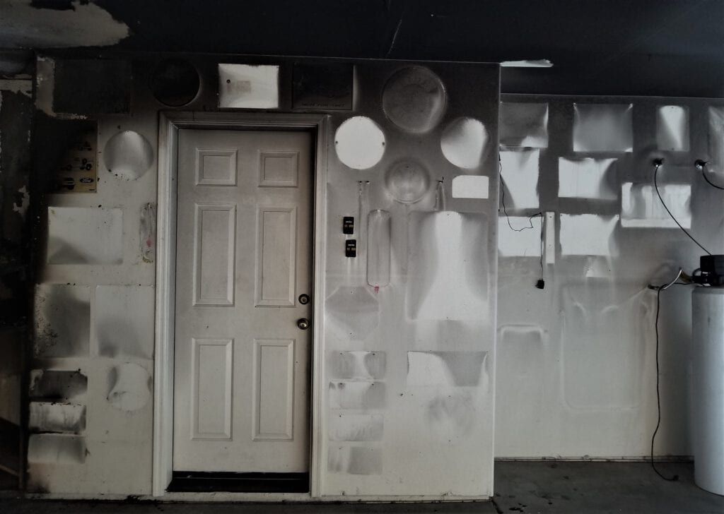 A white door is in a room with lots of fire and smoke damage. 