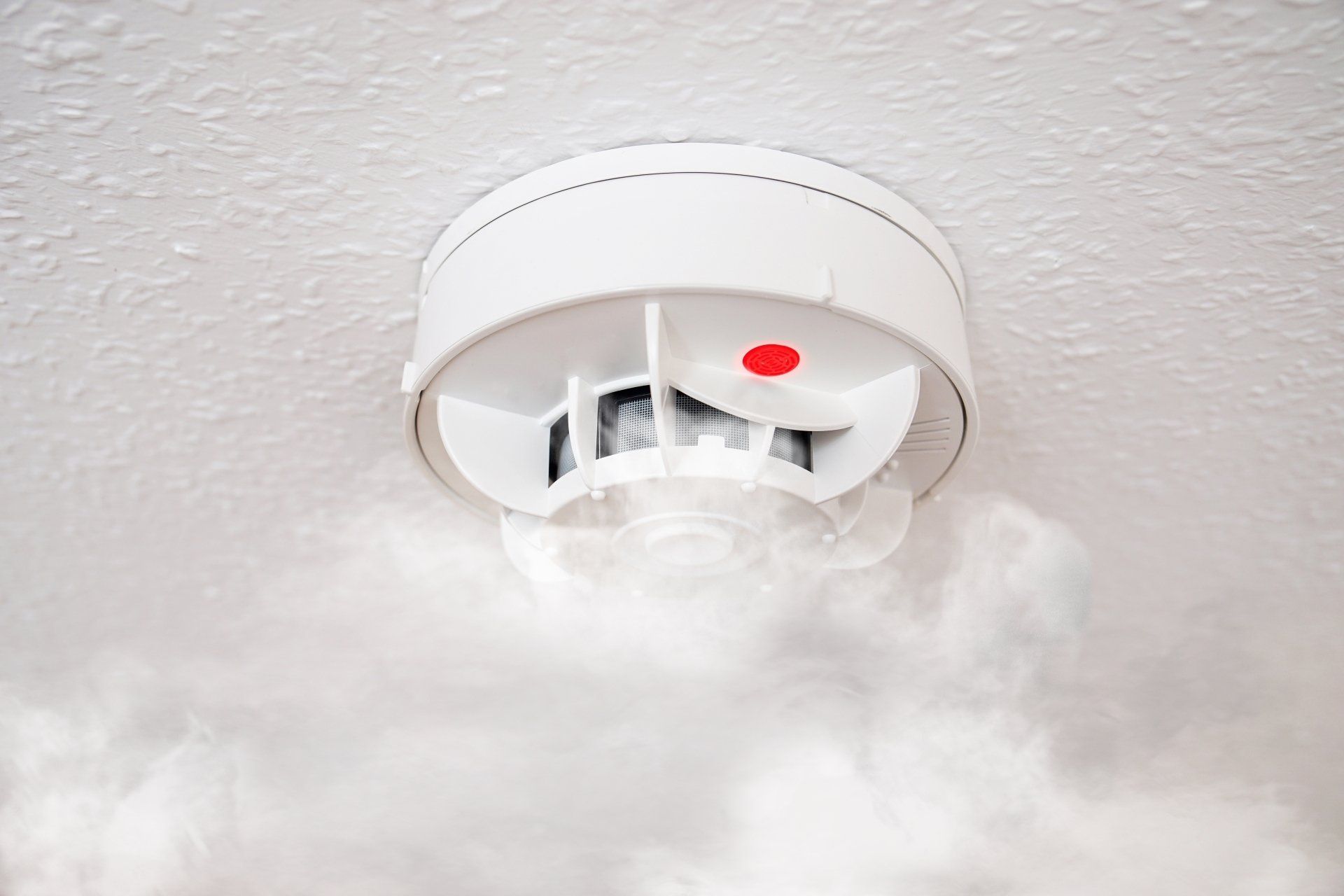 A smoke detector on the ceiling with smoke around it.