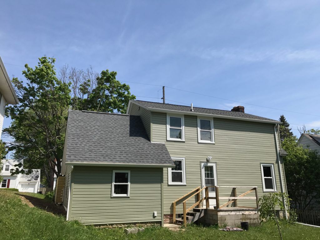 A green house with a gray roof is sitting on top of a grassy hill.