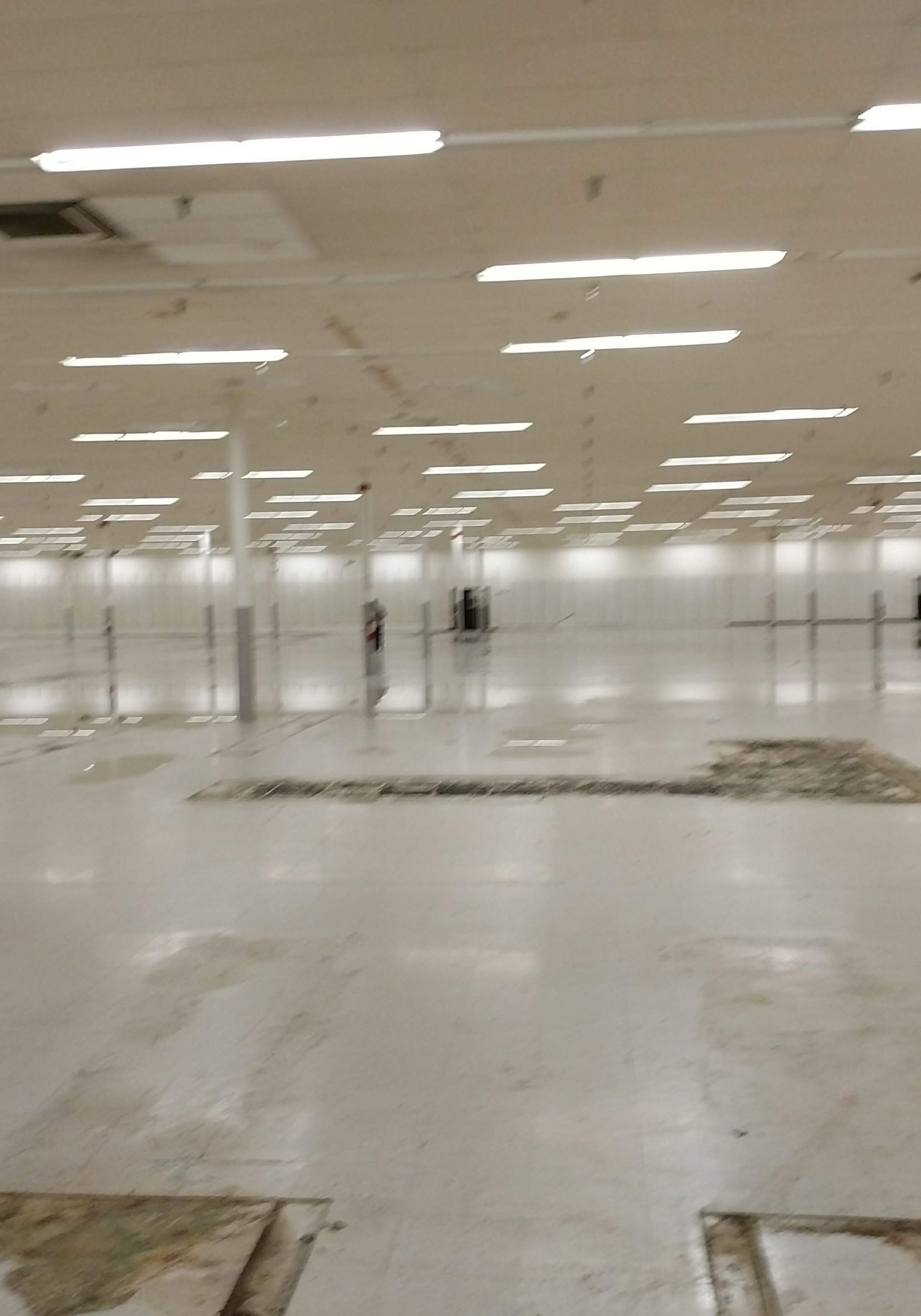 A large empty room with a lot of lights on the ceiling and damage on the floor. 