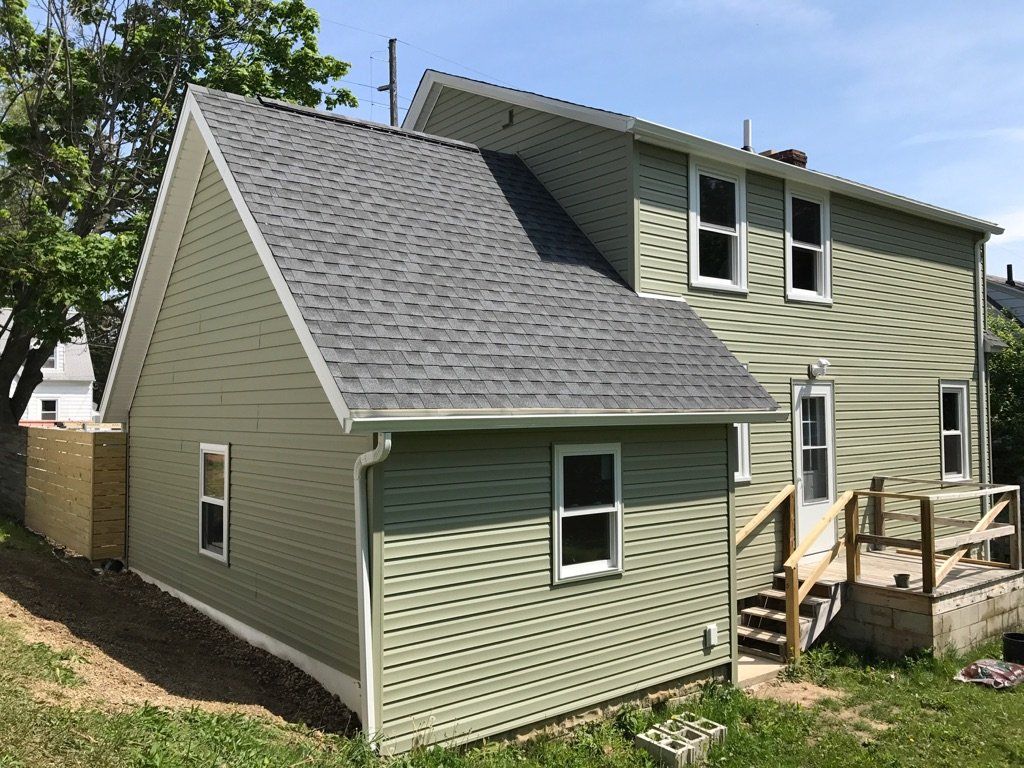 A green house with a gray roof and a deck.