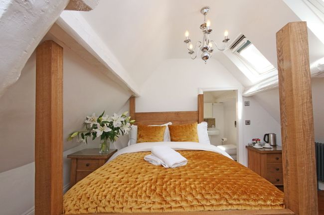 Bedroom with a bed, wooden beams, and a chandelier. Yellow bedding and a vase of white flowers add color.