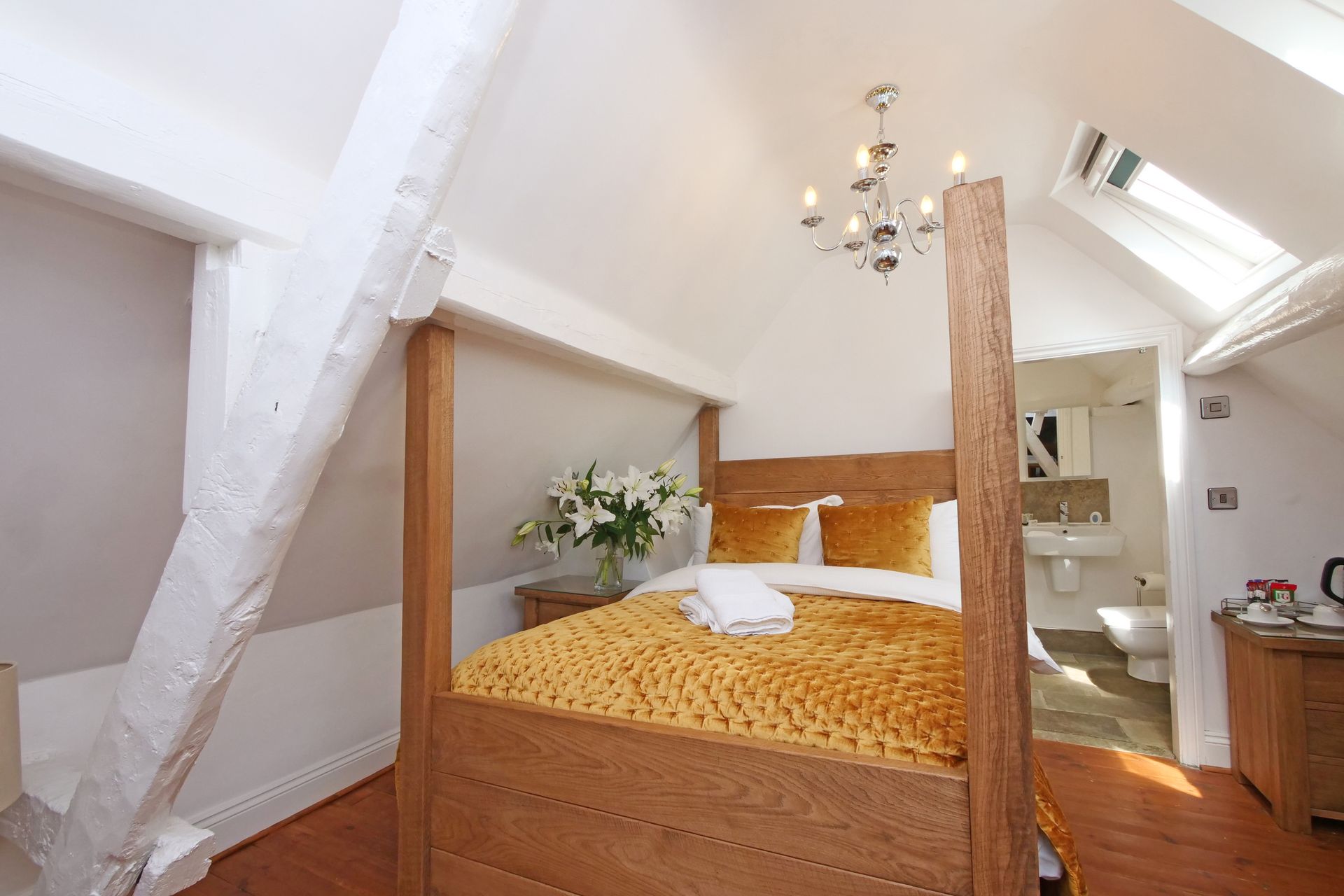 Bedroom with a four-poster bed, wooden beams, and a small ensuite bathroom. The bed has yellow blankets and pillows.
