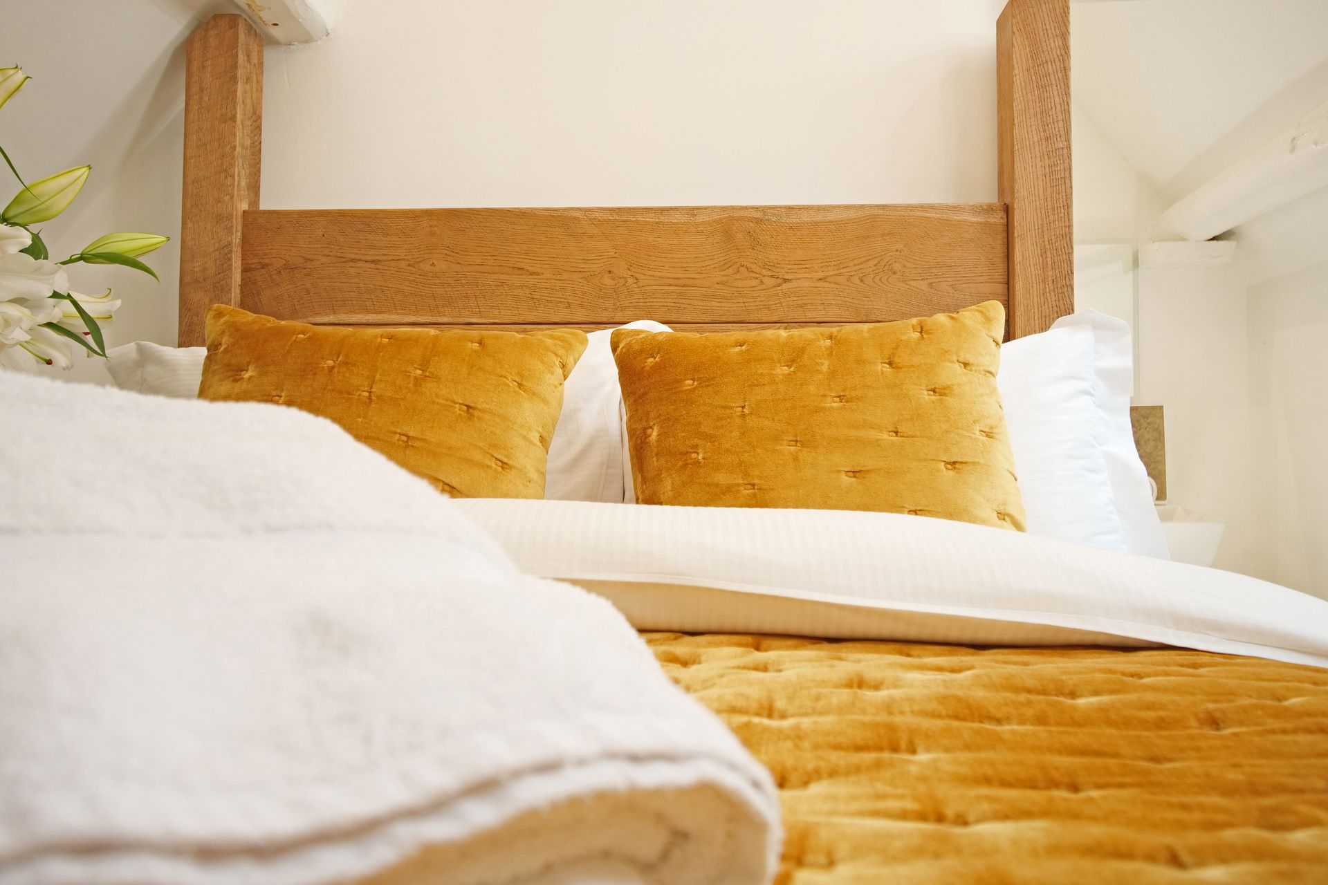 Wooden bed with yellow pillows and quilt, white bedding, and a neutral-toned room.