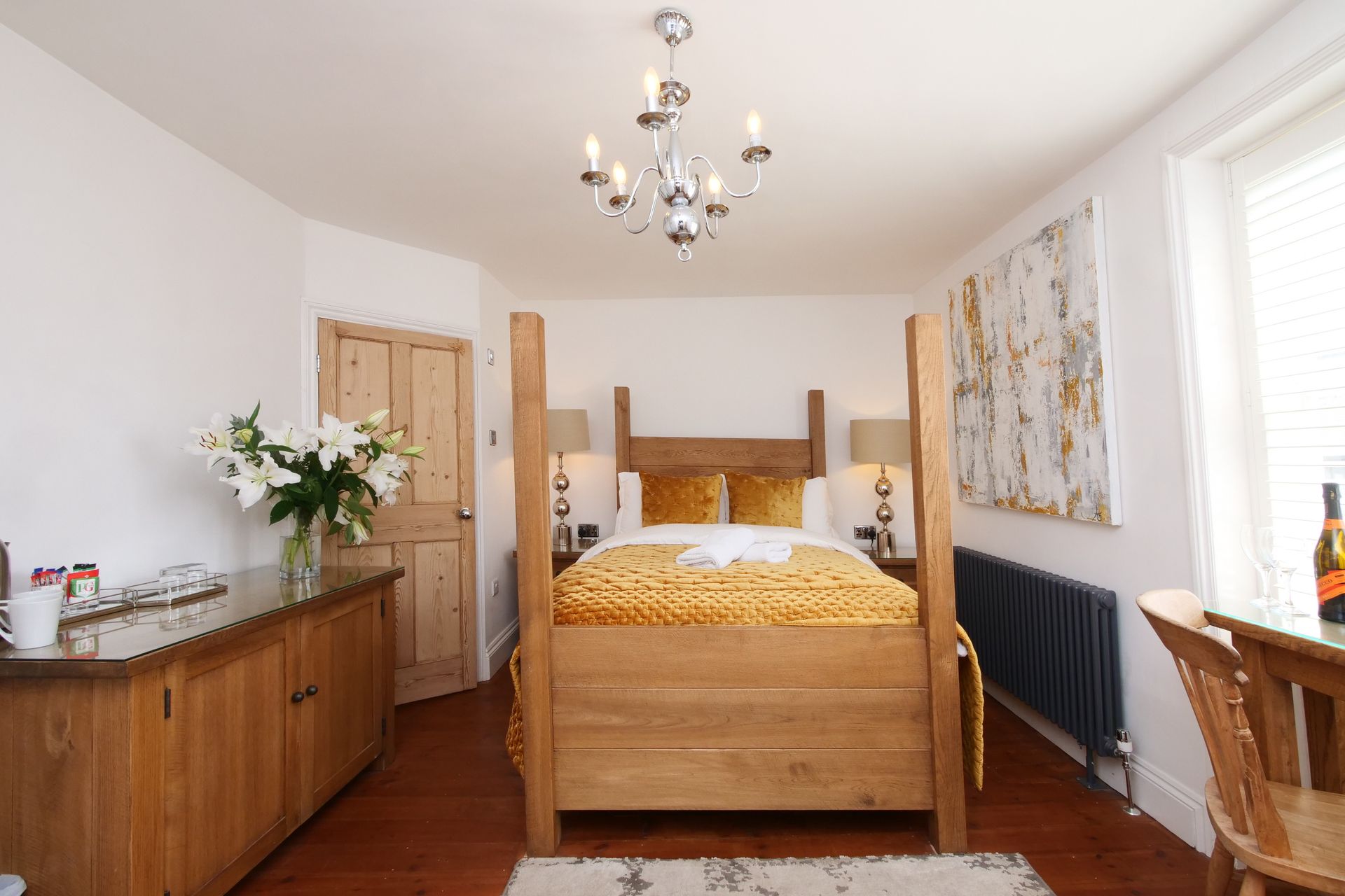 Bedroom with a four-poster bed and wooden furniture. Features a white wall, chandelier, and large window.